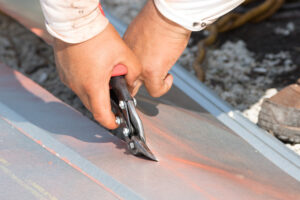 A roofer using sheers is working on a metal roof replacement.)