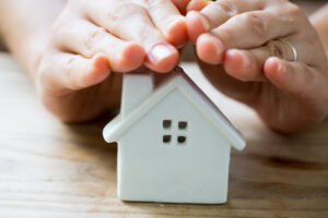 An image of a toy house with hands held over the roof representing the protection that a home roof warranty provides.